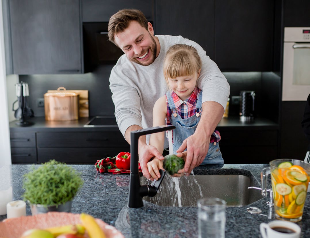 A parent and child washing a vegetable in the kitchen